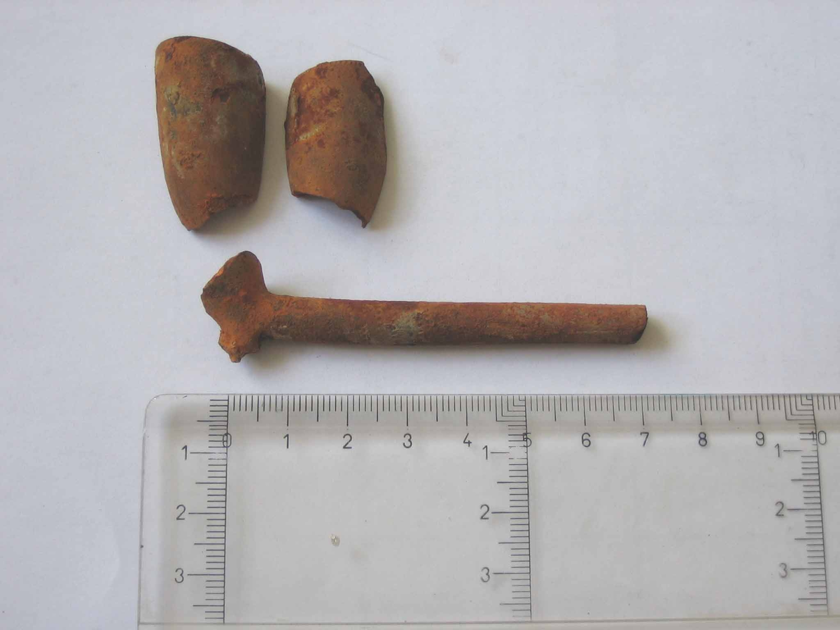 Punktornamentik i band runt skaftets nedre del samt svag punktornamentik runt  huvudets mynning. I tre delar.