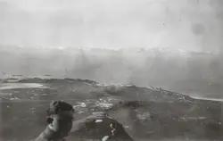 Mann ser i kamera, sitter på et høydedrag med blikk på Bø på