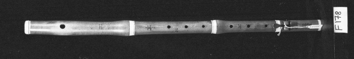 Tvärflöjt i buxbom med ringar av elfenben. 4 delar. Något konisk. Tydliga spår efter användning, särskilt vid anblåsningshålet. 1 silverklaff med bocklagring och kvadratisk platta.