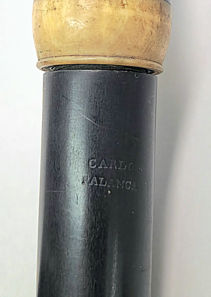 Tvärflöjt i ebenholts med ringar i horn/ben. 4 delar. 1 klaff med vulstlagring och oval platta. Översta ringen saknas och den nedersta ringen är sprucken. 