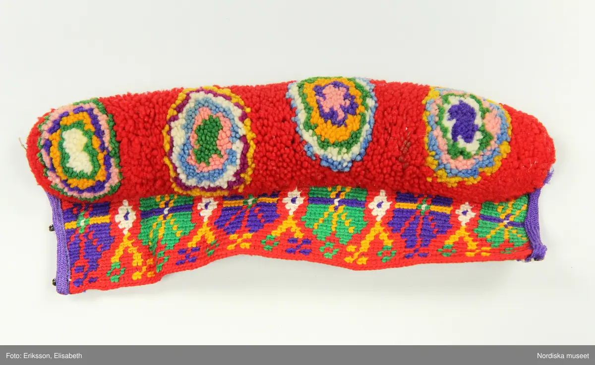 A-B. Muddar för man, ett par.
Maskinspunnet ullgarn, ylleband, hakar och hyskor.
Muddarna är virkade med fasta maskor med nedtag i bakre maskbågen i s.k. flerfärgsvirkning.  Mönstervirkningen görs hela tiden från rätsidan och garnet tas av för varje nytt varv. Kortsidorna är kantade med lila ylletrikåband, på den ena en rad maskinsöm. Det täta flossabrämet är sytt direkt i virkningen tråd för tråd och sedan formklippt. Knäpps runt handleden med tre svarta hakar och hyskor.
Färgerna är starka och opåverkade trots att det är kemiska s.k. anilinfärger som vanligtvis bleks mycket lätt.
/Berit Eldvik 2002