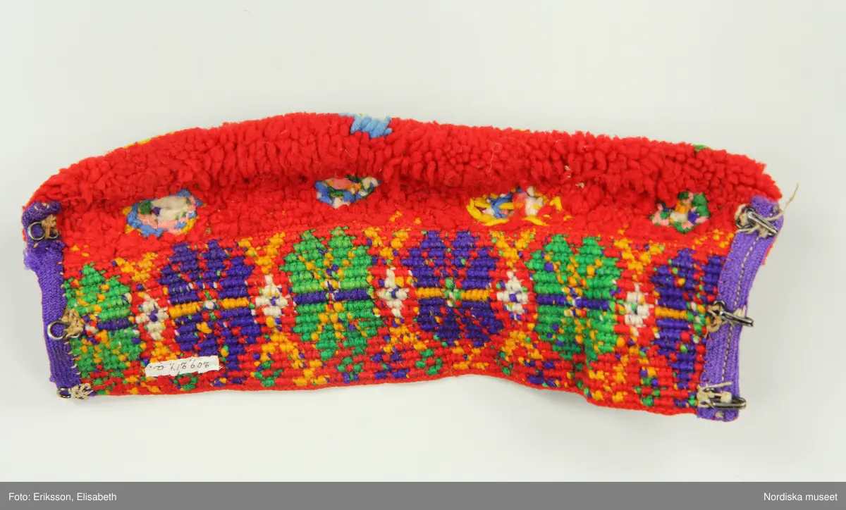 A-B. Muddar för man, ett par.
Maskinspunnet ullgarn, ylleband, hakar och hyskor.
Muddarna är virkade med fasta maskor med nedtag i bakre maskbågen i s.k. flerfärgsvirkning.  Mönstervirkningen görs hela tiden från rätsidan och garnet tas av för varje nytt varv. Kortsidorna är kantade med lila ylletrikåband, på den ena en rad maskinsöm. Det täta flossabrämet är sytt direkt i virkningen tråd för tråd och sedan formklippt. Knäpps runt handleden med tre svarta hakar och hyskor.
Färgerna är starka och opåverkade trots att det är kemiska s.k. anilinfärger som vanligtvis bleks mycket lätt.
/Berit Eldvik 2002