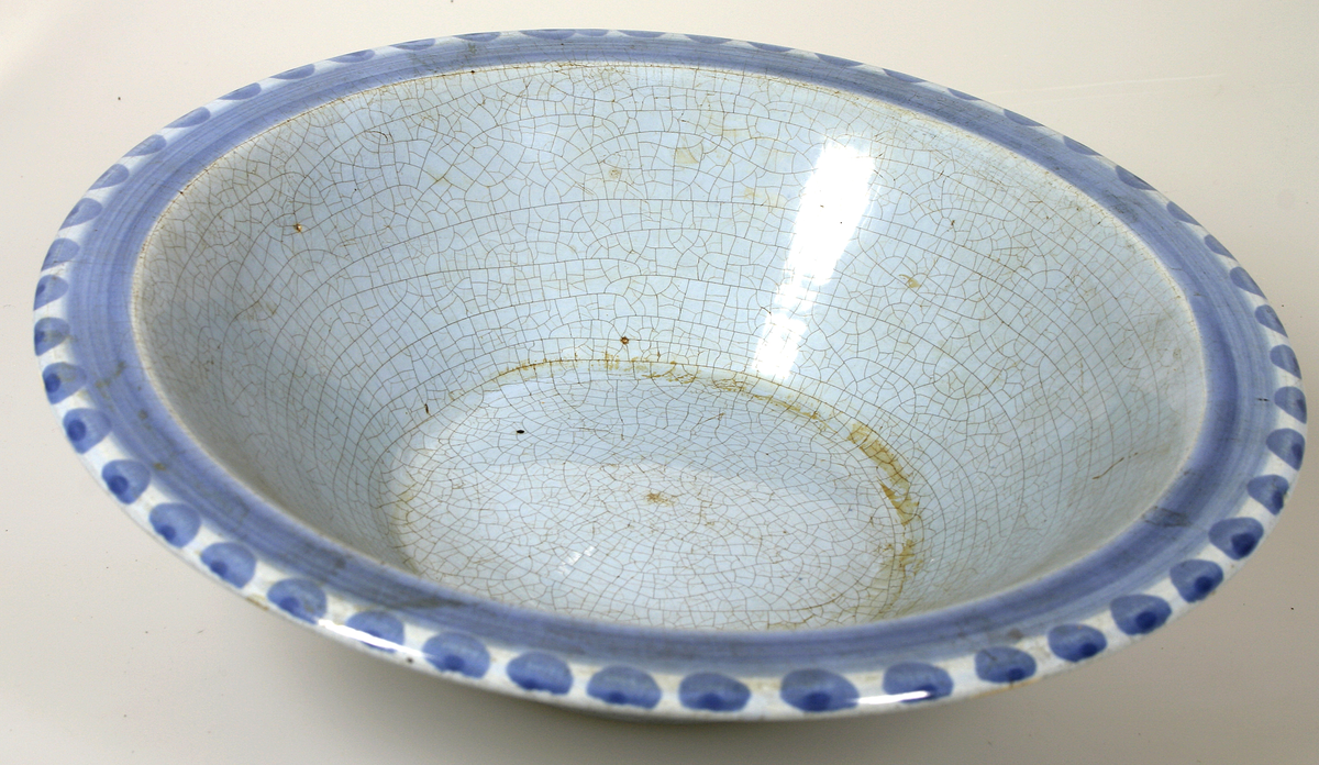 Skål av ljusblåglaserad lergods med målad dekor i mörkare blått.