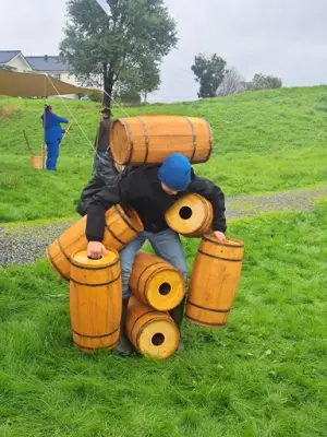 Ungdom forsøker å bære syv små tønner, mellom bein, over nakken, i hender og armer