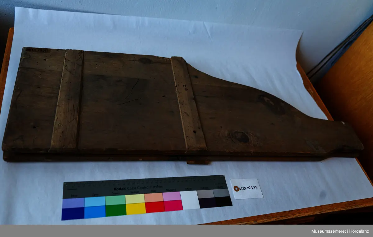 Bukseformer i tre. Kan brettes i to, Ble antakeligvis brukt til å tørke og forme ferdige underbukser før salg. Den har to hengsler.
Har to innfelte forsterkninger i tre, på tvers.