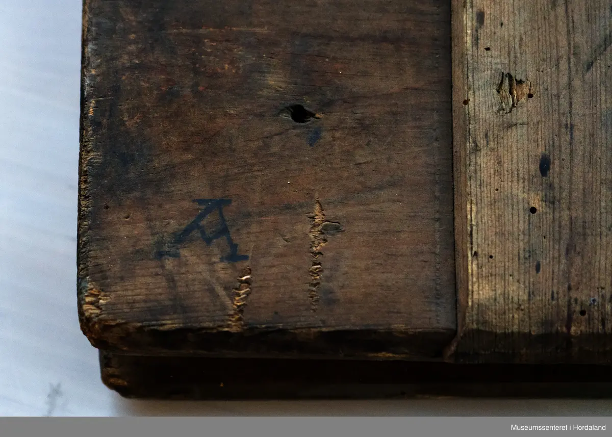 Bukseformer i tre. Kan brettes i to, Ble antakeligvis brukt til å tørke og forme ferdige underbukser før salg. Den har to hengsler.
Har to innfelte forsterkninger i tre, på tvers.