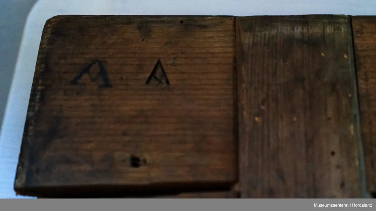 Bukseformer i tre. Kan brettes i to, Ble antakeligvis brukt til å tørke og forme ferdige underbukser før salg. Den har to hengsler.
Har to innfelte forsterkninger i tre, på tvers.