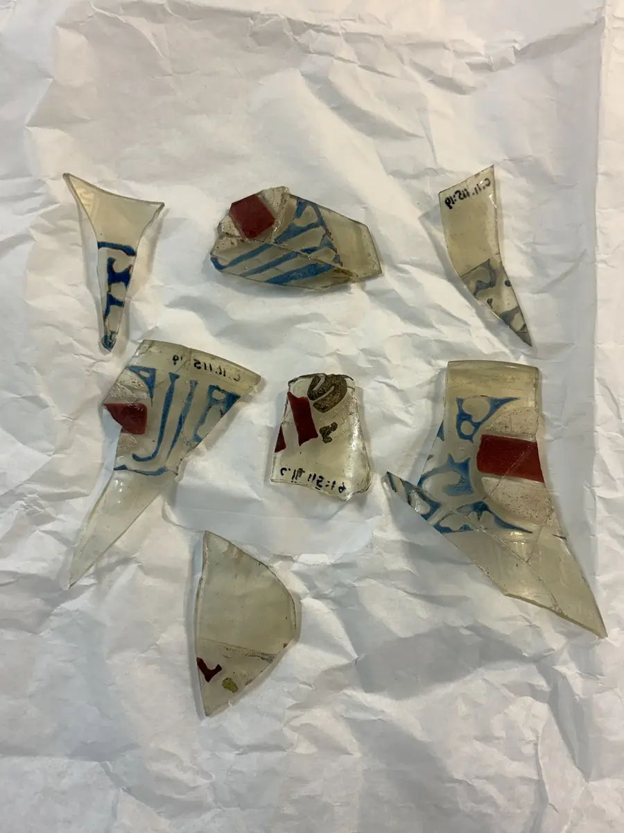 
Spår av röda, blå och vita färger, överst arabisk inskrift. 
Hela ytan är graverad med slingor, som troligtvis varit täckta med guld, och ur denna bakgrund framträder tre mänskliga figurer vars kläder varit dels emaljerade i rött och vitt, dels belagda med guld, som vid fyndet redan fallit bort. På glasets brätte finns tre vapensköldar som antyder att ägaren varit emir och mellan dessa en arabisk inskrift, som lytt: "Ära vare vår herre, sultanen, konungen , den rättvise, den vise, ära vare hans seger." Samma inskrift upprepas omedelbart under brättet. 

Nuvarande höjd 19, övre diam. C:a 11, nedre diam. C:a 6 cm. Inskrift översatt till svenska: "ära vare vår herre, sultanen, konungen, den rättvise, den vise, ära vare hans seger". 