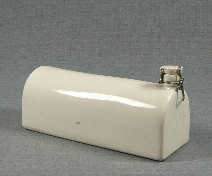 Värmekrus av vitt porslin. I ena kortsidan mynning med patentkork.