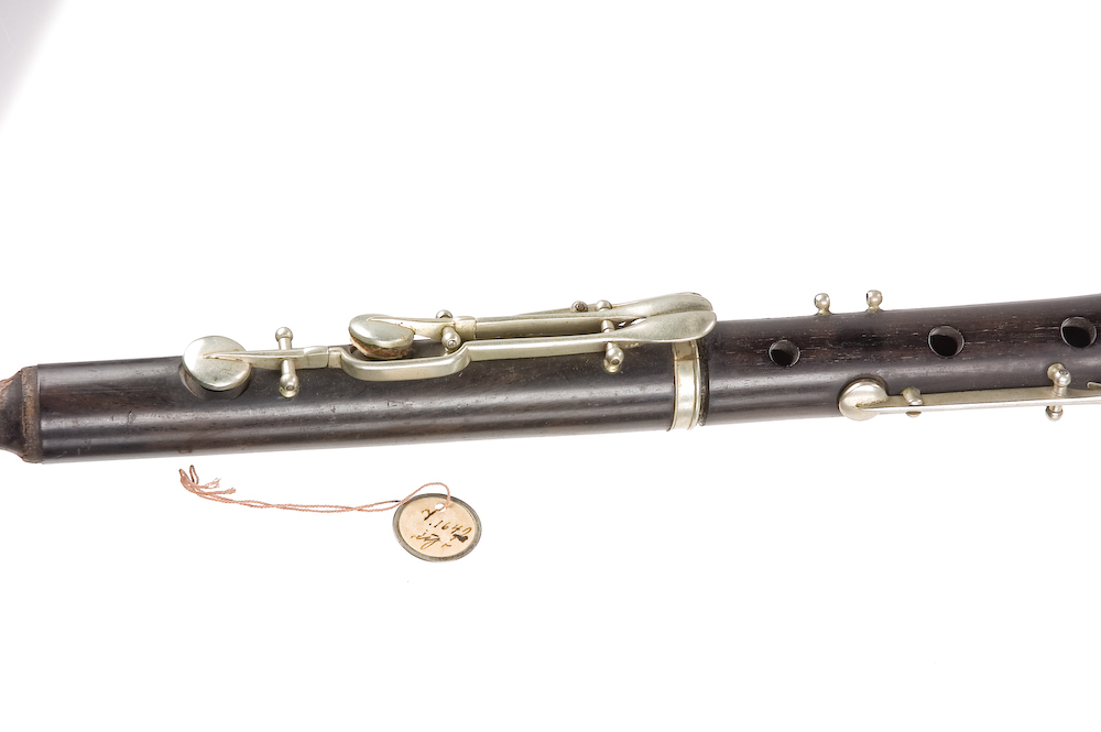 Tvärflöjt i mörkt trä med silverringar. 5 delar. Konisk form. Något krökt. Nedersta ringen saknas. 8 klaffar med kullagring och runda plattor, varav 1 klaff saknas. Sprickor i munstycke och päron. Nedre mellanstycke sprucket och amatörmässigt lagad.
