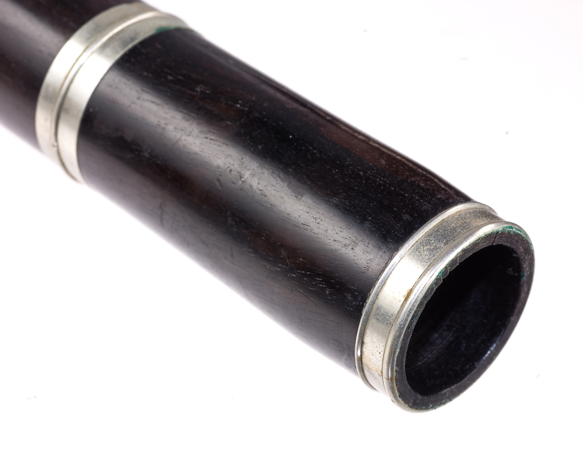 Tvärflöjt i mörkt trä med silverringar. 5 delar. Konisk form. Något krökt. Nedersta ringen saknas. 8 klaffar med kullagring och runda plattor, varav 1 klaff saknas. Sprickor i munstycke och päron. Nedre mellanstycke sprucket och amatörmässigt lagad.