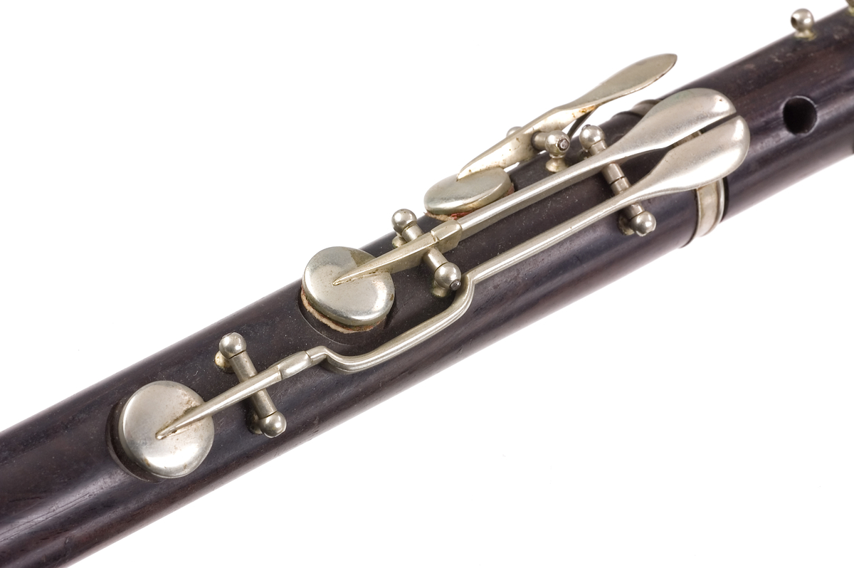 Tvärflöjt i mörkt trä med silverringar. 5 delar. Konisk form. Något krökt. Nedersta ringen saknas. 8 klaffar med kullagring och runda plattor, varav 1 klaff saknas. Sprickor i munstycke och päron. Nedre mellanstycke sprucket och amatörmässigt lagad.