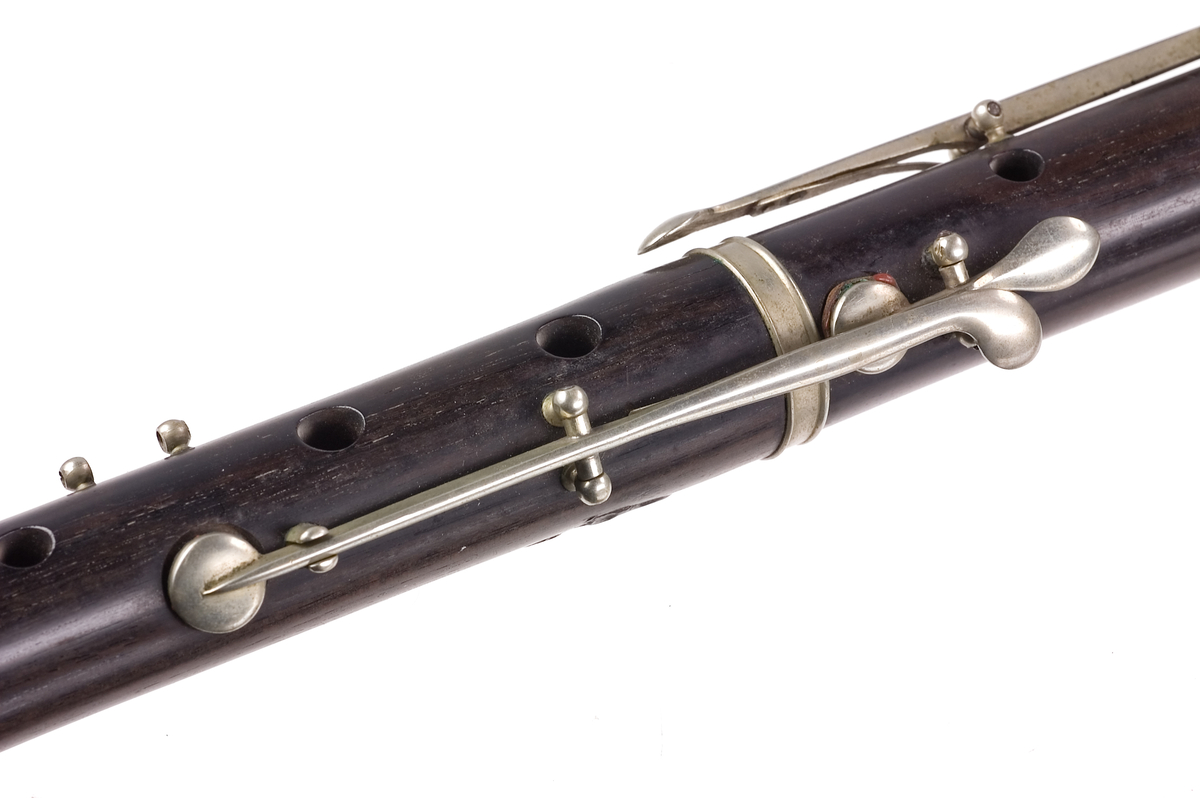 Tvärflöjt i mörkt trä med silverringar. 5 delar. Konisk form. Något krökt. Nedersta ringen saknas. 8 klaffar med kullagring och runda plattor, varav 1 klaff saknas. Sprickor i munstycke och päron. Nedre mellanstycke sprucket och amatörmässigt lagad.