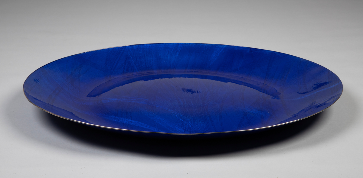 Fat i sølv med pålagt emalje. Sirkulær form med svakt hvelvet bunn og jevnt oppbuede sider. Over- og undersiden er dekket med blå emalje på frest bunn. Mønster i form av strålebunter som buer fritt over overflaten.