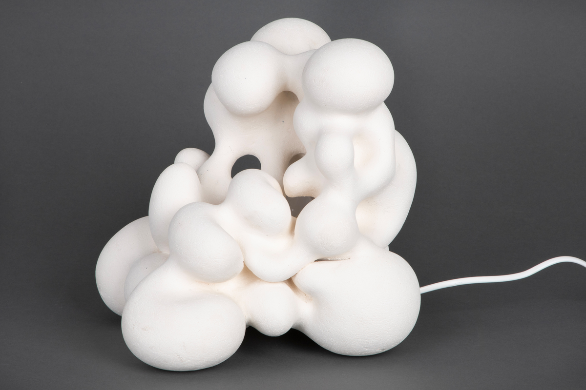 Hvit lampe i porselen. Formet av sammensmeltede bobleformer. Rund, gul lyspære inni, lyskilden er synlig fra utsiden. Skjult kabelfeste bak.