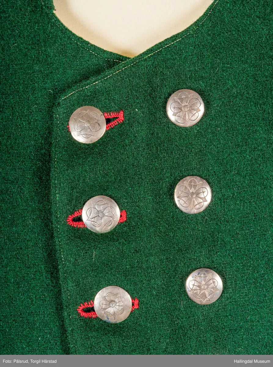Vest til mann i grønn vadmel. Smal kanting i same stoff langs halsopningen. Dobbeltspent, 7 par knappar med fembladsrose festa med skinnlist. Knapphol sydd med raud ulltråd. 

Stikklomme med klaff på kvart forstykke. Lukking med knapp med fembladsrose, festa med skinnlist. På klaffen er knapphol med broderi i plattsaum over. Klaffen er forsterka med regels på kvar side. Knapphol, regels og prydsaum er sydd med raud ulltråd. 

Belegg langs framkant og nedkant på framstykke av kypervevd stoff. Sidesaum med splitt. Skuldersaum på skulder. Rygg i grønn vadmel. Saum midt bak, med raudt broderi over. 