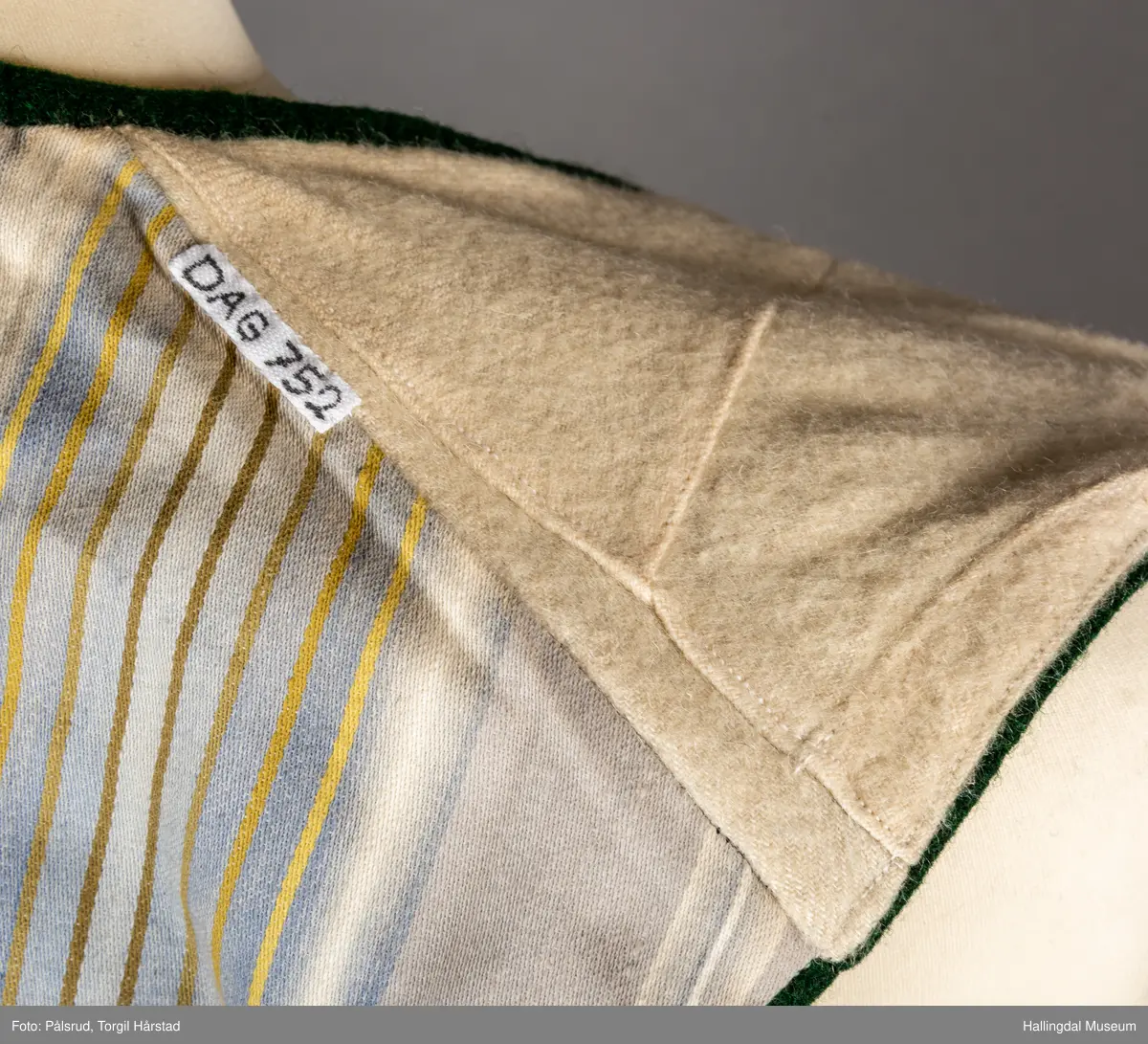 Vest til mann i grønn vadmel. Smal kanting i same stoff langs halsopningen. Dobbeltspent, 7 par knappar med fembladsrose festa med skinnlist. Knapphol sydd med raud ulltråd. 

Stikklomme med klaff på kvart forstykke. Lukking med knapp med fembladsrose, festa med skinnlist. På klaffen er knapphol med broderi i plattsaum over. Klaffen er forsterka med regels på kvar side. Knapphol, regels og prydsaum er sydd med raud ulltråd. 

Belegg langs framkant og nedkant på framstykke av kypervevd stoff. Sidesaum med splitt. Skuldersaum på skulder. Rygg i grønn vadmel. Saum midt bak, med raudt broderi over. 