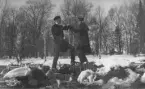 Två unga män står lekfullt stridspositionerade vid ett gäng stenar täckta av snö och is. Männen är iklädda rock och huvudbonad. Bilden är troligt tagen i en park under 1910-1920 tal.