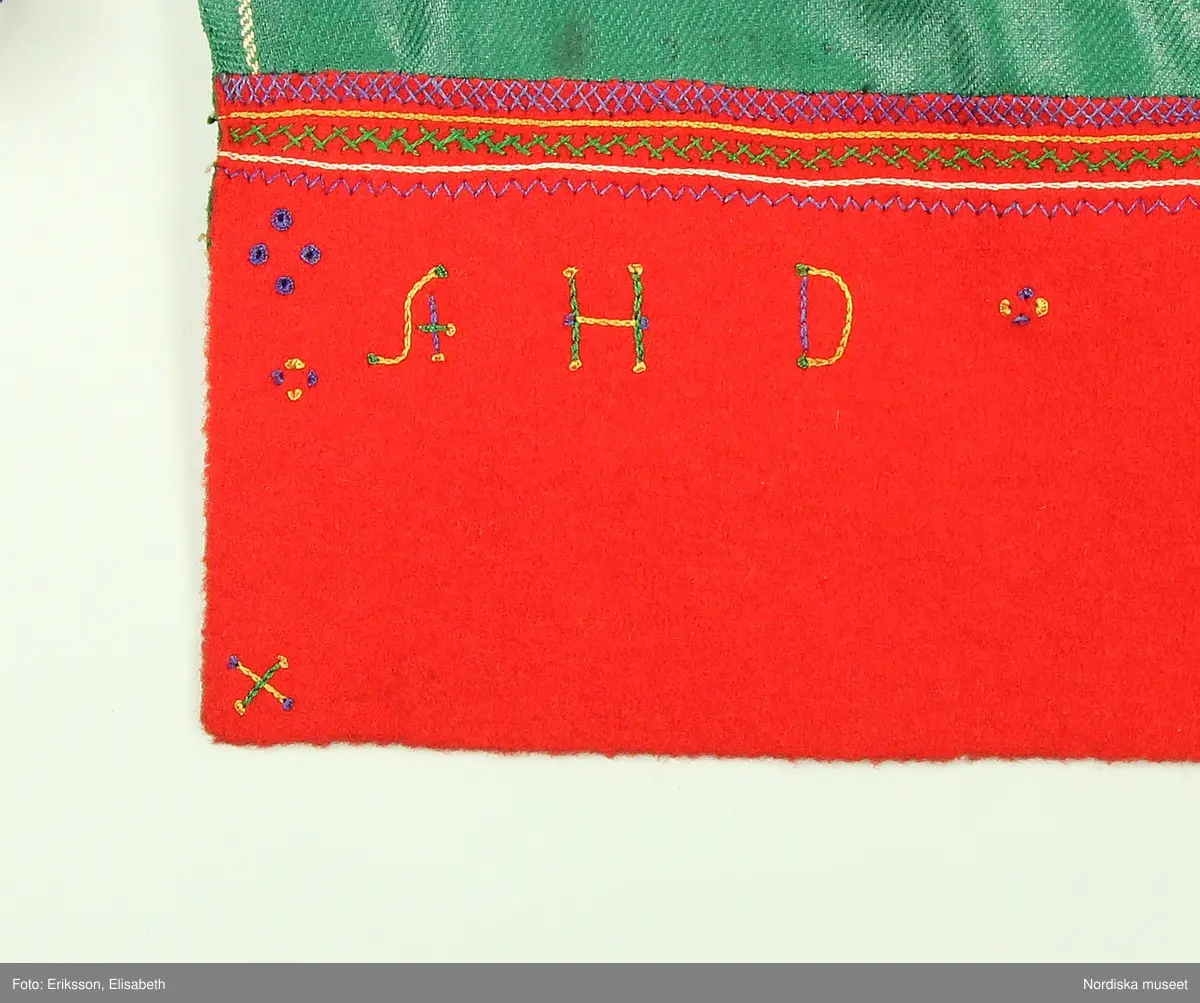 Huvudliggaren:
"Kvinnodräkt fr. Orsa sn, OfvanSiljans fgd, Dalarna.
a. Kjol med lif
b. Tröja         b. Sönderrifven å bakstycket.
c. Förkläde. Märkt: 'AHD 1854'
d. Öfverdel  [tecknat bomärke]
e. Halskläde [tecknat bomärke]
f. Strumpor
g. Skor
h. Band 5 st      h. valk, överklädd metalltråd
i. Hufvudkläde
j. Handskar
k. Bokkläde
l. Bjällernål. Af silver
m. Psalmbok. Tryckt i Göteb 1883."

Bilaga:
Finns ej.

Katalogkort:
Inga ytterligare uppgifter.

A. Livkjol,
Liv av högrött ylle med fågelmönster, importerat tyg trol engelskt av hög kvalitet, mitt fram kring öppningen  applikation av rött kläde med flerfärgat silkebroderi.4 par snörmaljor av tenn. Snörband av ljusbrunt skinn. Kjol av svartbrunt halvylle.
B. Tröja av svart kläde, lång modell. Sömmar sydda på maskin, stickningar runt kanterna för hand, nederkant och ärmuppslag har rå avklippt kant utan fåll.
Anm. Tröjan är helt ny och oanvänd, troligen uppsydd på beställning för förvärvet till museet för att få ihop en hel dräkt. Inte heller  psalmboken som ingår är gammal, den har tryckår 1883. Säljaren var en av Hazelius s.k. skaffare. Det var inte ovanligt att delar plockades ihop på bygden för att få ihop till en hel dräkt för museets räkning. 
Anm. I huvudliggaren står att litt b. är sönderriven  i ryggen, vilket inte stämmer.
/Berit Eldvik 2010-11-04

C. Förkläde "Glansmagd"
Av grön rask, nedtill en röd klädeslist som är broderad med silke i flera färger samt märkt AHD 1854.
D. Överdel. Smal utdragssöm över axeln med lila tråd markerar var ärmen börjar, ärmen avslutas med knäppta rynkor mot ärmlinning med nuggor i kanten och ett påsytt ca 1 cm brett mönstervävt band i blått och vitt. Enkelt halssprund utan knäppning.
/Berit Eldvik  2005-05

E: Halskläde i vit tuskaftad bomull . Parallella rynkningar med knäppning mot 5 cm hög rak krage som viks. Kragen prickar i langettsöm, bård i trädsöm, två rader efterstygn, nuggor utmed långsida,  Iträtt tuskaftsvävt knytband i rött och vitt, bred bård i gul, vit och rosa (fällningar) stopphålssöm, myrgångsbårder i kanterna. Dalknypplad spets fastsydd i framkant. Fållar maskinsydda för övrigt handsydd.
/Inga-Lill Eliasson 2007-08-01

K. Vitt kvadratiskt bokkläde i bomull, kypertdräll, rombiska former. Två stadkanter med gul tråd och två maskinsydda fållar.
/Inga-Lill Eliasson 2007-08-13