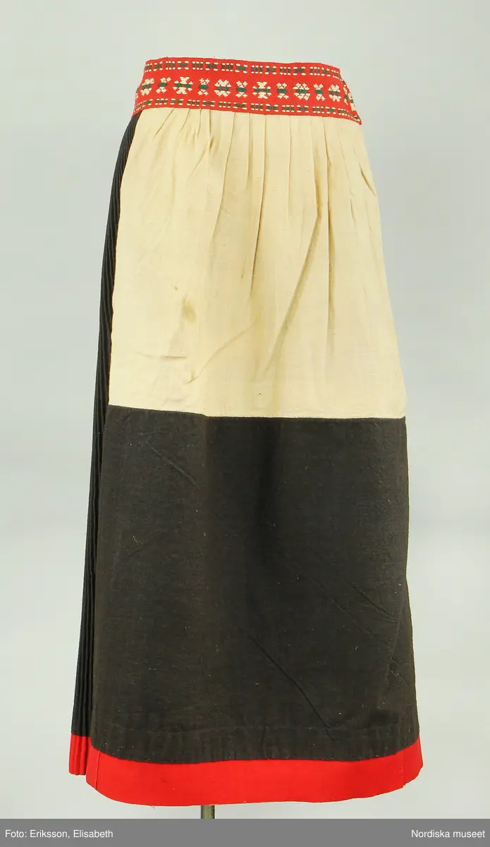 Huvudliggaren:
"Kvinnodräkt fr. Delsbo sn, Norra Helsinglands fgd, Helsingland.
a. "Ryntjeskjortel" af svart kläde med röd kant och bandväfd "kval" (linning). Kjolen "lurad"(goffrerad), skall förvaras lurad att ej vecken gå ut. 3 par fruntimmershänder hjälpas åt att "lura" den efter hvarje begagnande.
b. livstycke, rött med gröna ränder.
c. "Ryntjessärk" (rynksärk) af hvitt bomullstyg med "krus" (handbroderi) kring hals och händer.Begagnas sommartiden
d. "Bumsförkläde" af ylle, blårandigt med bandväf,"kval" i rödt och grönt.
e. "Förklesband" rödt och grönt ylle med "doppar" (tofsar) i ändarna. Lindas 1 à 2 hvarf kring lifvet och bindes framtill med stora nedhängande "locor" och ändar. Längd 262 cm, bredd 3,4 cm.
f. Kjolsäck med mässingslås och hake samt tennbroderi. Häktas under förklesbandet och hänger delvis under "försklet". Begagnas vanligen till förvaring af kyrkkryddor m.fl. kyrk-ellerkalassaker.
g. Halfhandskar af svart kläde med silkesbroderi. Begagnas sommartiden.
h. "Påshufva" hvardagsmössa af brokigt kattun. Begagnas med i nacken utslaget hår med några hårtestar hängande fritt framför öronen.
Till dräkten användes röda strumpor samt låga skor med höga klackar. Äfven kan användas silfersmycken kring halsen eller å  bröstet. En á två brokiga silkesdukar brukades omkring halsen nedstoppade under lifstycket, så att kruset kring halsen  på "ryntjessärken" sammanfästadt med ett löfspänne samt en smalare kant af hvarje sidenduk, blevo synliga. Vid handlederna sammanfästes ryntjessärken med röda sidenband eller länkknappar.

a. KJOL 
längd: 87 cm
midjeband bredd: 7 cm
av svart halvylle med svart linvarp och inslag av svart 1-tr. ullgarn, de 2 yttersta stadtrådarna är av oblekt lingarn. 4 goffrerade våder samt en slät framvåd som skarvats under förklädet med oblekt bomullslärft. 5 cm bred list av rött kläde i nederkanten runtom. Brett midjeband mönstervävt i rött och grönt ullgarn och vitt bomullsgarn. Knäppt vid framvådens vänstra sida med 2 hakar och hyskor av mässing.
b. LIVSTYCKE
längd: 39 cm
av halvylle i varptäckande kypert, varp av vitt lingarn, inslag av svart och grönt ullgarn med flaminslag av vitt, 2 fram-och sidstycken, 2 bakstycken avsmalnande till skörtveck med tre par tränsade förstärkningar av svart garn. I midjehöjd ett avsytt veck runtom, knäppt kant i kant med 8 par grova hakar och hyskor av mässing. Foder av ofärgad bomullslärft.
BE

c. ÖVERDEL
Längd: 39 cm. Längd: 58 cm - ärmlängd. Vidd: 56 cm - ärmvidd. Vidd: 114 cm. Höjd: 1,7 cm - kraghöjd. Material: Textil, bomull. Textil, linne - ärmlinning, krage. Bomullsgarn - broderi. Telnik: Tuskaft. Trådbundet broderi. Broderi, rätlinjig plattsöm. Handsömnad.
Överdel av tuskaftat vitt bomullstyg. Dubbelvikt bålstycke, isydda rektangulära halsspjäll. Täta breda stripade  rynkor mot halskrage i bomull, 1,7 cm hög. Kragen har broderier i rätlinjig plattsöm, vitt bomullsgarn över hela ytan, nuggor i kanten, langetterade bågar  i framkant. 16 cm långt sprund fram, tränsad förstärkning nedtill, 3 cm.  Vidsydd ärm med  infällda ärmspjäll, lagda veck över axeln fram och bak. Täta breda stripade rynkor mot 2,5 cm bred ärmlinning. Ärmlinningen har yttäckande vita broderier i rätlinjig plattsöm, rombiska former. Vita knytband i bomull i ärmlinningar och krage. Överdelen är handsydd.
/Inga-Lill Eliasson 2007-11-26


d. FÖRKLÄDE
längd=vådbredd: 82 cm
bredd: 97,5 cm
av halvylle, varp av svart lingarn, inslag i varptäckande kypert av svart 1-tr. ullgarn med smala ränder istarkt blått och en knappt synlig svart tråd med vita flamgarnsfläckar av bomull. Upptill stripade rynkor där de blå bårderna utnyttjats dekorativt i rynkningen. Mönstervävt midjeband i grönt på rött ullgarn , bandet knäpps med 2 hakar och hyskor i vänster sida.
I nederkantens båda hörn infodringar på insidan av svart bomullslärft, för att tyget inte skall rulla sig.



Berit Eldvik 2004