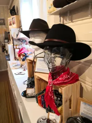 To sorte cowboyhatter er utstilt på glasshoder. Rundt hallesn ad det ene en rød bandana, den andre et lisseslips. Andre præriesaker kan skimptes på et velfullt langt bord langs veggen