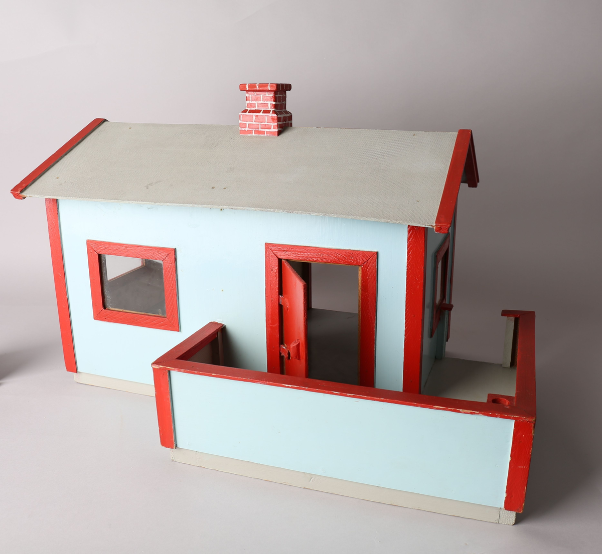 Rektangulært hus med påbygget veranda. Huset er malt lys blått med røde lister utvendig, innvendig tapet i brunbeige med hvite organiske striper og beide tapet med motiv av vegetasjon og blomster i hvitt, grønt og rødlige farger. Gulvet er malt grått og taket innvendig er umalt. Innvendige lister i trehvitt. Grått tak med rød pipe med påmalte hvite striper for å etterligne murstein. Sett forfra er dør ut til veranda i det venstre rommet. Innebygget kasse til flaggstang i venstre hjørne på veranda med avtagbar flaggstang. Norskt flagg heiset til topps i flaggstangen.
