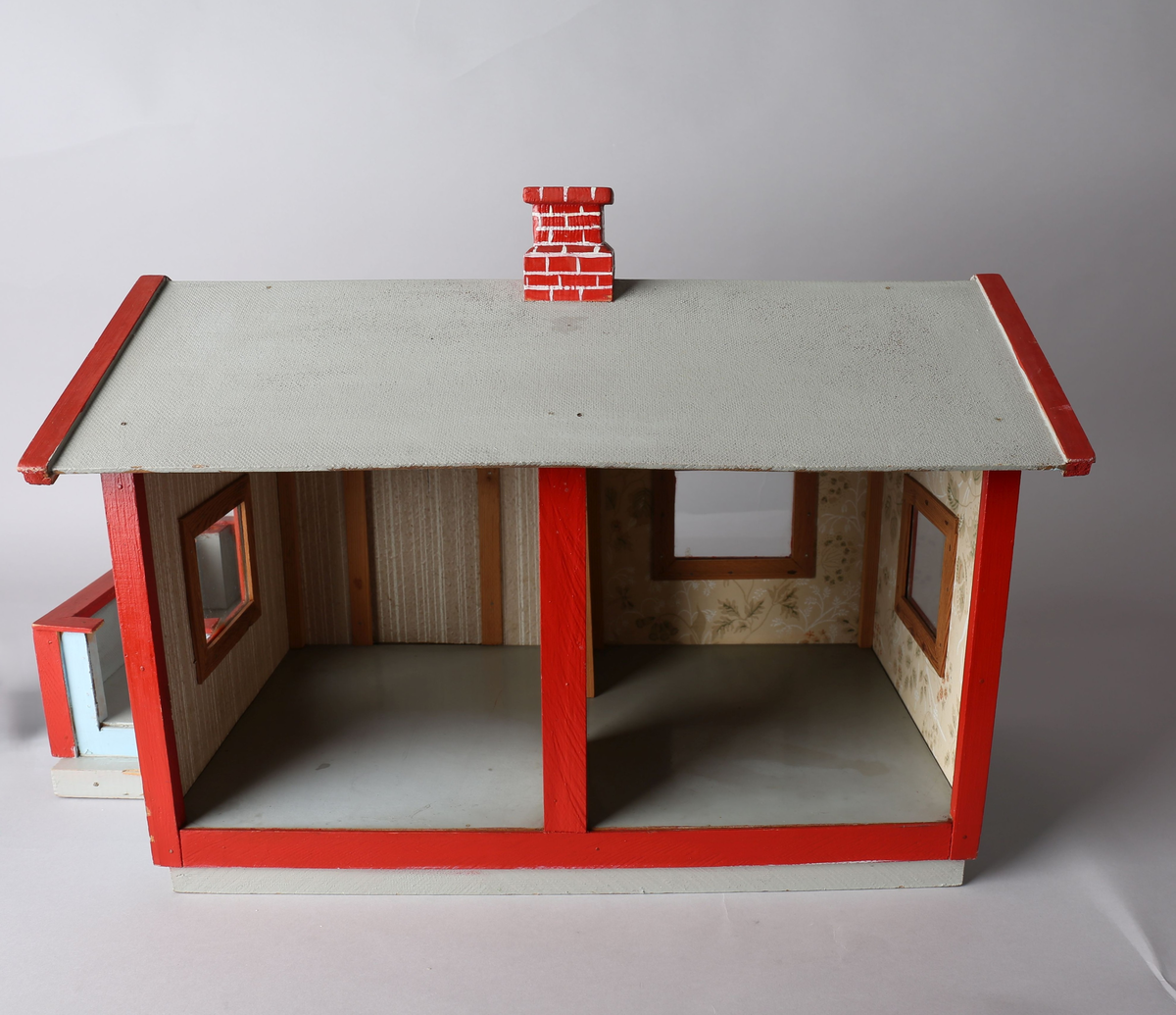 Rektangulært hus med påbygget veranda. Huset er malt lys blått med røde lister utvendig, innvendig tapet i brunbeige med hvite organiske striper og beide tapet med motiv av vegetasjon og blomster i hvitt, grønt og rødlige farger. Gulvet er malt grått og taket innvendig er umalt. Innvendige lister i trehvitt. Grått tak med rød pipe med påmalte hvite striper for å etterligne murstein. Sett forfra er dør ut til veranda i det venstre rommet. Innebygget kasse til flaggstang i venstre hjørne på veranda med avtagbar flaggstang. Norskt flagg heiset til topps i flaggstangen.
