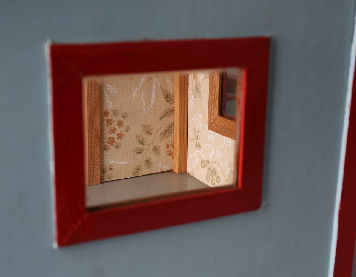 Rektangulært hus med påbygget veranda. Huset er malt lys blått med røde lister utvendig, innvendig tapet i brunbeige med hvite organiske striper og beide tapet med motiv av vegetasjon og blomster i hvitt, grønt og rødlige farger. Gulvet er malt grått og taket innvendig er umalt. Innvendige lister i trehvitt. Grått tak med rød pipe med påmalte hvite striper for å etterligne murstein. Sett forfra er dør ut til veranda i det venstre rommet. Innebygget kasse til flaggstang i venstre hjørne på veranda med avtagbar flaggstang. Norskt flagg heiset til topps i flaggstangen.
