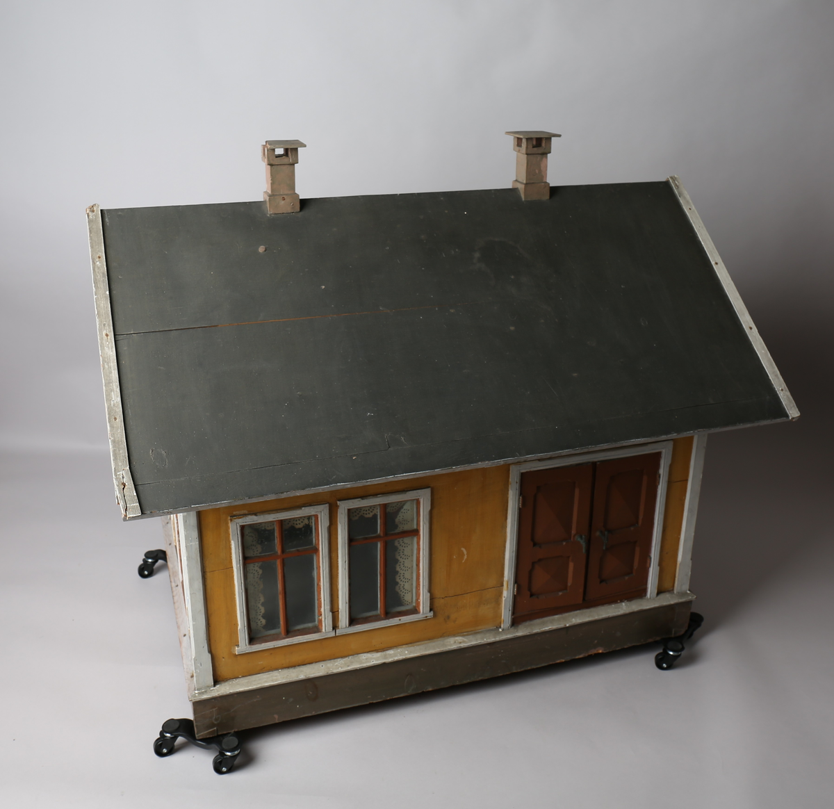 Rektangulært dukkehus i treverk med fire faste vegger. Huset består av fire rom og åpen loftsetasje. Totalt har huset ti vinduer og to doble dører som fungerer som enkeltdører. Utvendig er huset malt gult med hvite lister og brune dører og sprosser. Innvendig er gulvene malt grå, veggene rosa og gule med hvite innvendige sprosser. Gardiner i hvitt blondepapir og papirbilder er festet på veggene med tegnestifter. Veggene på loftet er malt mintgrønn.