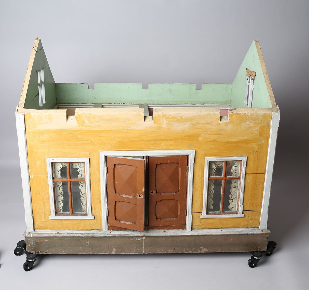 Rektangulært dukkehus i treverk med fire faste vegger. Huset består av fire rom og åpen loftsetasje. Totalt har huset ti vinduer og to doble dører som fungerer som enkeltdører. Utvendig er huset malt gult med hvite lister og brune dører og sprosser. Innvendig er gulvene malt grå, veggene rosa og gule med hvite innvendige sprosser. Gardiner i hvitt blondepapir og papirbilder er festet på veggene med tegnestifter. Veggene på loftet er malt mintgrønn.