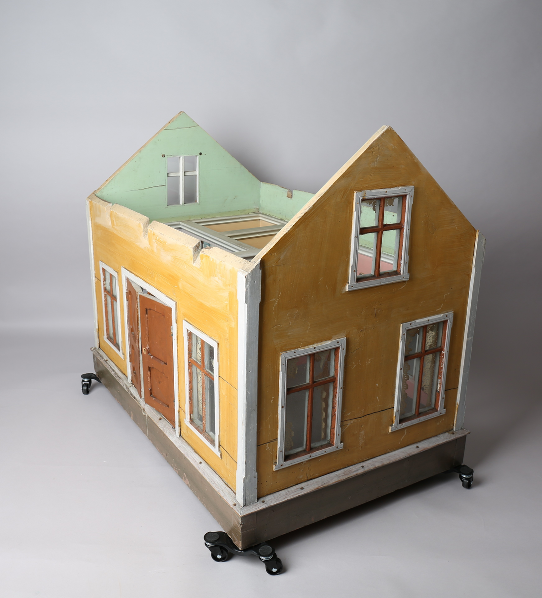 Rektangulært dukkehus i treverk med fire faste vegger. Huset består av fire rom og åpen loftsetasje. Totalt har huset ti vinduer og to doble dører som fungerer som enkeltdører. Utvendig er huset malt gult med hvite lister og brune dører og sprosser. Innvendig er gulvene malt grå, veggene rosa og gule med hvite innvendige sprosser. Gardiner i hvitt blondepapir og papirbilder er festet på veggene med tegnestifter. Veggene på loftet er malt mintgrønn.