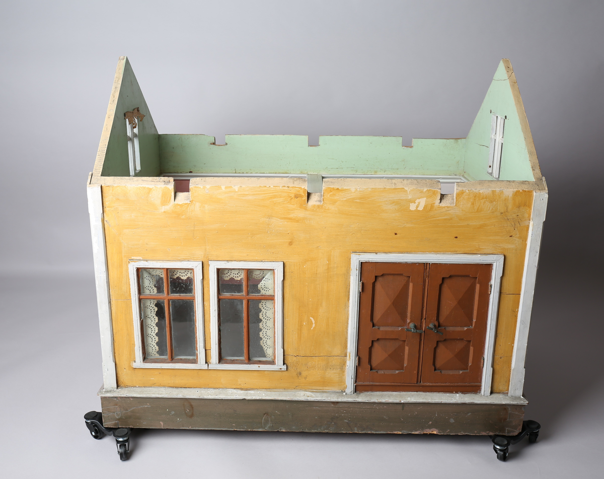 Rektangulært dukkehus i treverk med fire faste vegger. Huset består av fire rom og åpen loftsetasje. Totalt har huset ti vinduer og to doble dører som fungerer som enkeltdører. Utvendig er huset malt gult med hvite lister og brune dører og sprosser. Innvendig er gulvene malt grå, veggene rosa og gule med hvite innvendige sprosser. Gardiner i hvitt blondepapir og papirbilder er festet på veggene med tegnestifter. Veggene på loftet er malt mintgrønn.