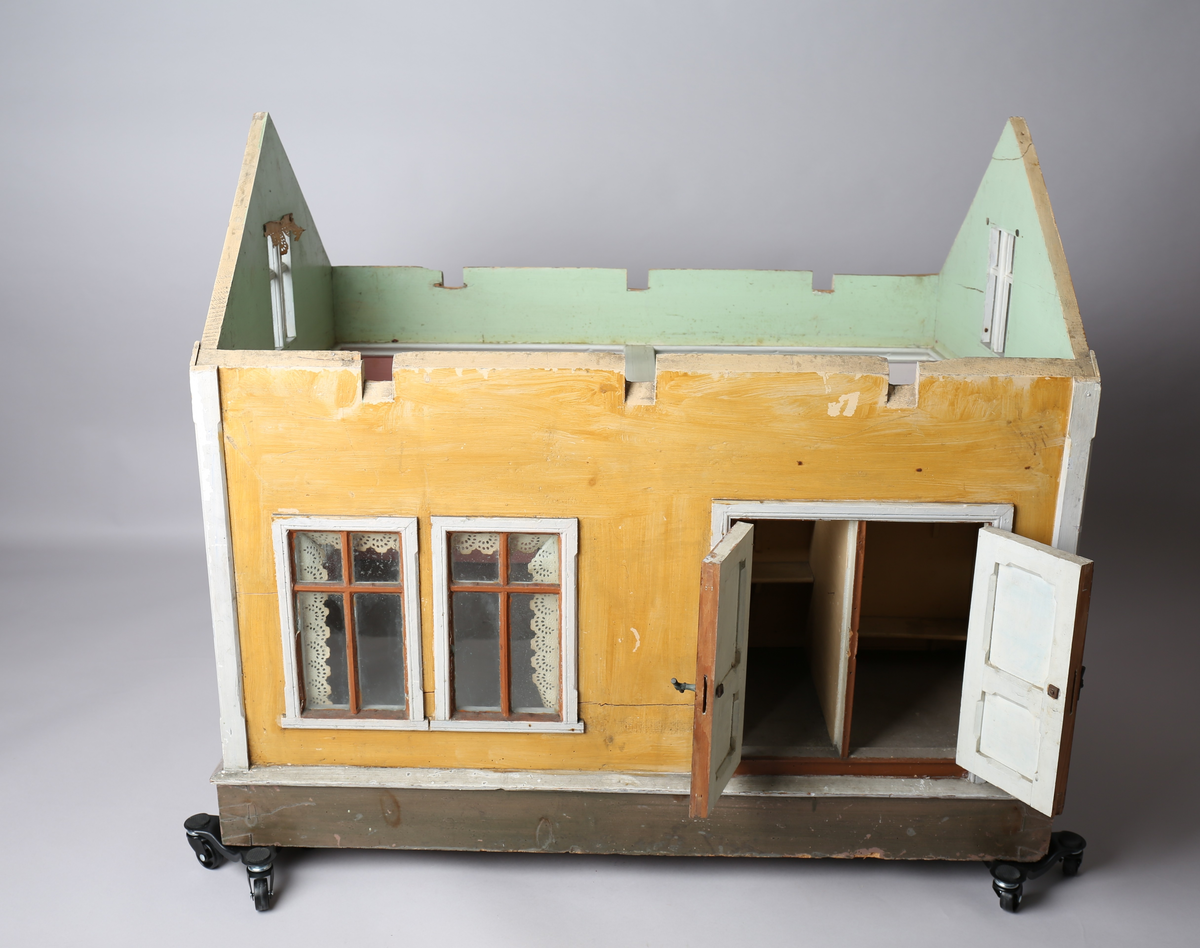 Rektangulært dukkehus i treverk med fire faste vegger. Huset består av fire rom og åpen loftsetasje. Totalt har huset ti vinduer og to doble dører som fungerer som enkeltdører. Utvendig er huset malt gult med hvite lister og brune dører og sprosser. Innvendig er gulvene malt grå, veggene rosa og gule med hvite innvendige sprosser. Gardiner i hvitt blondepapir og papirbilder er festet på veggene med tegnestifter. Veggene på loftet er malt mintgrønn.