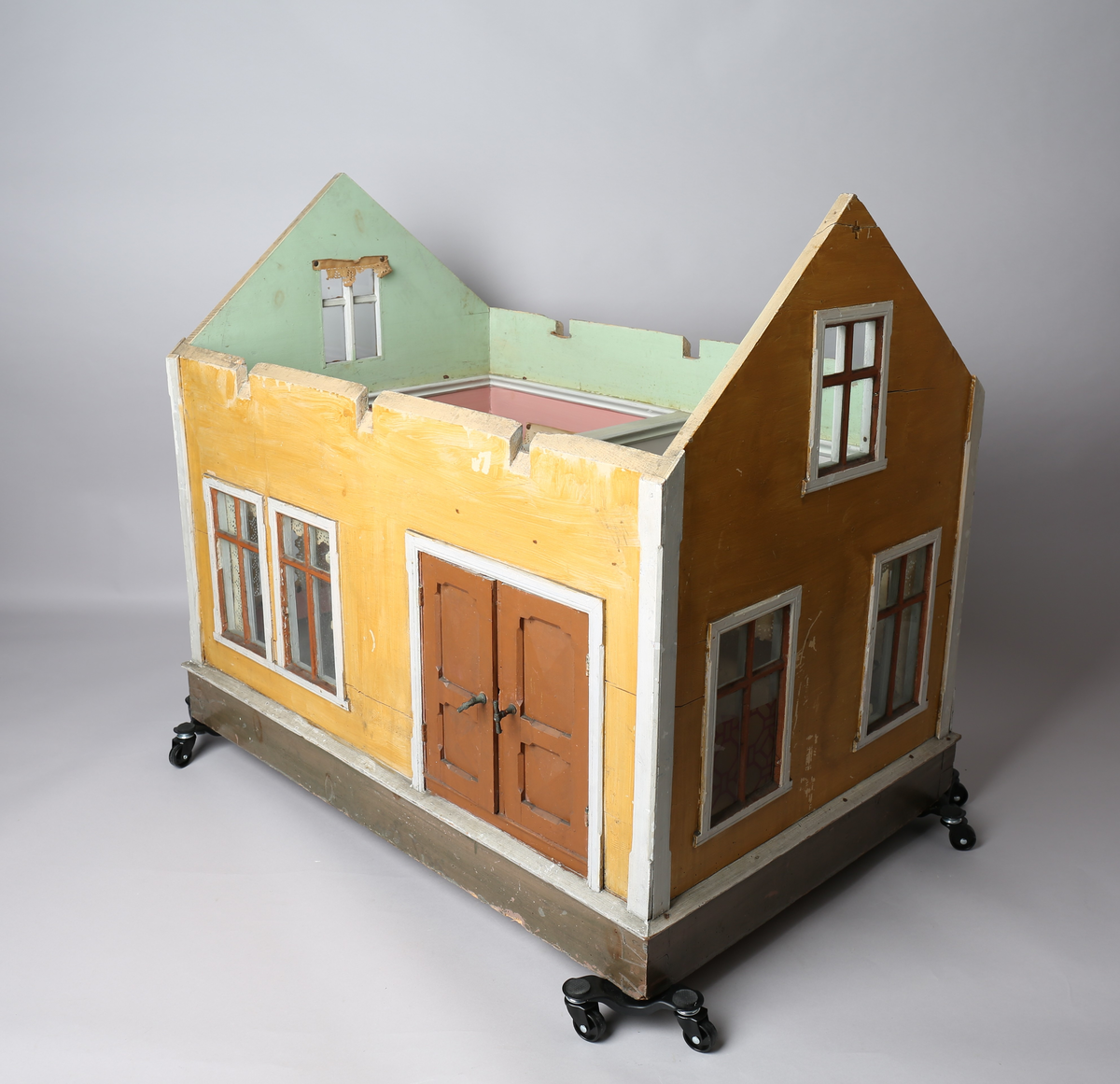 Rektangulært dukkehus i treverk med fire faste vegger. Huset består av fire rom og åpen loftsetasje. Totalt har huset ti vinduer og to doble dører som fungerer som enkeltdører. Utvendig er huset malt gult med hvite lister og brune dører og sprosser. Innvendig er gulvene malt grå, veggene rosa og gule med hvite innvendige sprosser. Gardiner i hvitt blondepapir og papirbilder er festet på veggene med tegnestifter. Veggene på loftet er malt mintgrønn.