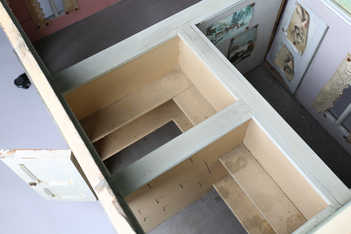 Rektangulært dukkehus i treverk med fire faste vegger. Huset består av fire rom og åpen loftsetasje. Totalt har huset ti vinduer og to doble dører som fungerer som enkeltdører. Utvendig er huset malt gult med hvite lister og brune dører og sprosser. Innvendig er gulvene malt grå, veggene rosa og gule med hvite innvendige sprosser. Gardiner i hvitt blondepapir og papirbilder er festet på veggene med tegnestifter. Veggene på loftet er malt mintgrønn.