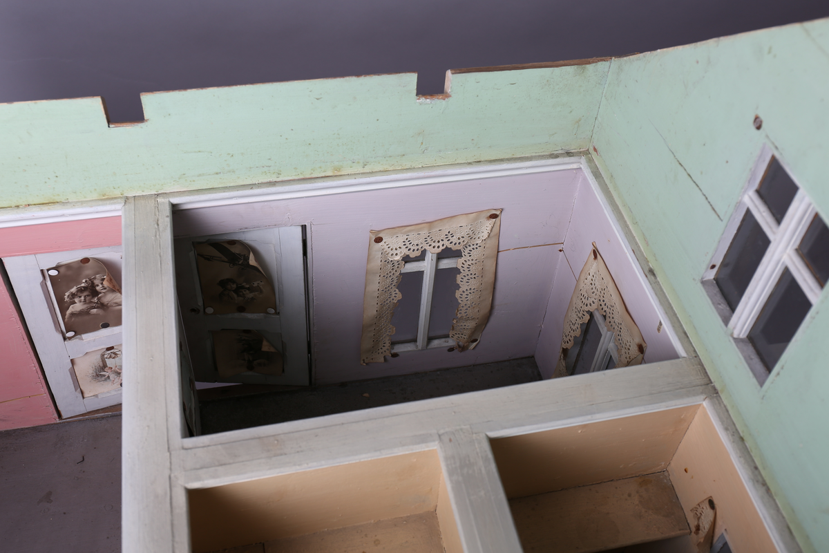 Rektangulært dukkehus i treverk med fire faste vegger. Huset består av fire rom og åpen loftsetasje. Totalt har huset ti vinduer og to doble dører som fungerer som enkeltdører. Utvendig er huset malt gult med hvite lister og brune dører og sprosser. Innvendig er gulvene malt grå, veggene rosa og gule med hvite innvendige sprosser. Gardiner i hvitt blondepapir og papirbilder er festet på veggene med tegnestifter. Veggene på loftet er malt mintgrønn.