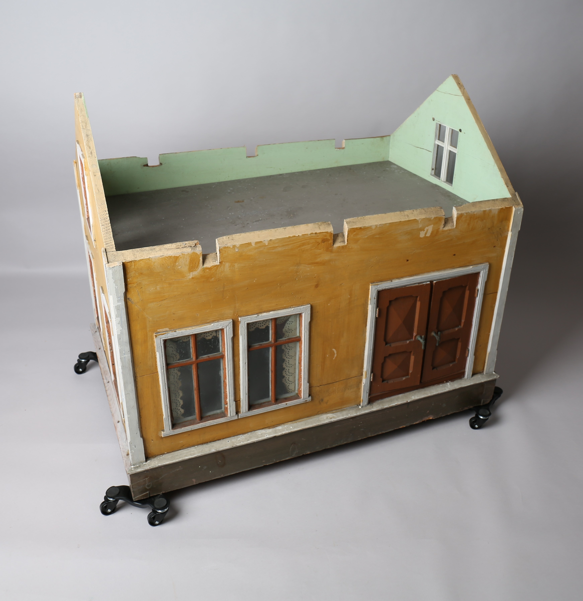 Rektangulært dukkehus i treverk med fire faste vegger. Huset består av fire rom og åpen loftsetasje. Totalt har huset ti vinduer og to doble dører som fungerer som enkeltdører. Utvendig er huset malt gult med hvite lister og brune dører og sprosser. Innvendig er gulvene malt grå, veggene rosa og gule med hvite innvendige sprosser. Gardiner i hvitt blondepapir og papirbilder er festet på veggene med tegnestifter. Veggene på loftet er malt mintgrønn.