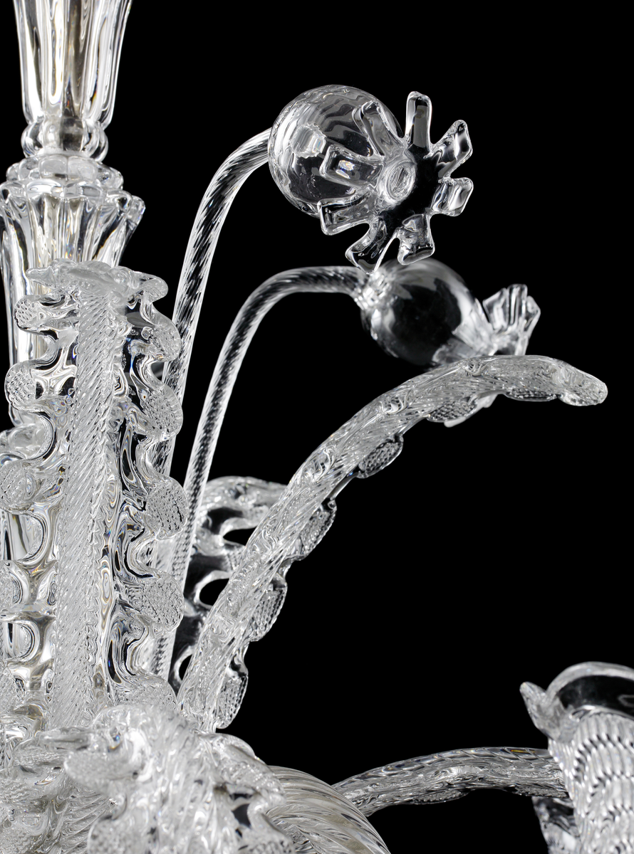 Takarmatur formgiven av Fritz Kurz. Underst en skål i pressat glas vari en infästningsanordning döljer sig. I denna sitter fem s-formade ljusarmar för elektriskt ljus placerade, tillsammans med sammanlagt tio stiliserade växt-dekorationer.