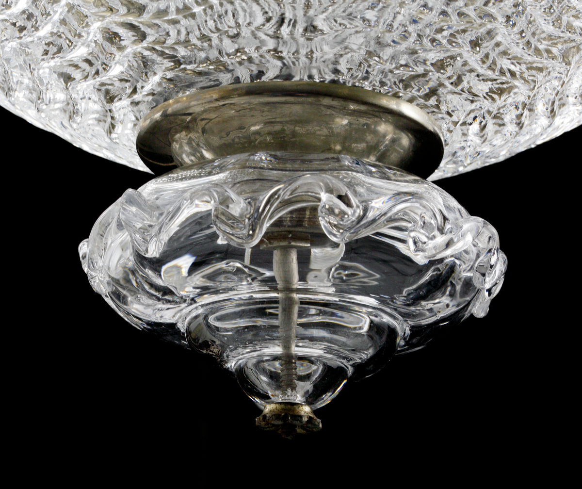 Takarmatur formgiven av Fritz Kurz. Underst en skål i pressat glas vari en infästningsanordning döljer sig. I denna sitter fem s-formade ljusarmar för elektriskt ljus placerade, tillsammans med sammanlagt tio stiliserade växt-dekorationer.