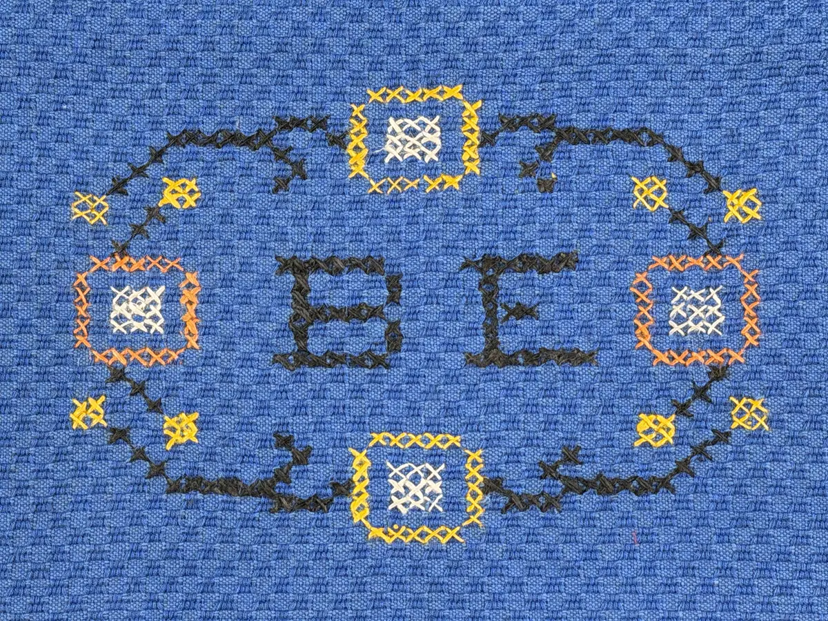 Tygpåse gjord av bomullsväv i sålldräll och broderi utfört med lingarn i korsstygn. Påsens öppning har en dragsko, 22mm bred dubbelvikt sydd med smygstygn, för förslutning med ett band. Påsen är hopsydd med vändsöm och raksöm.