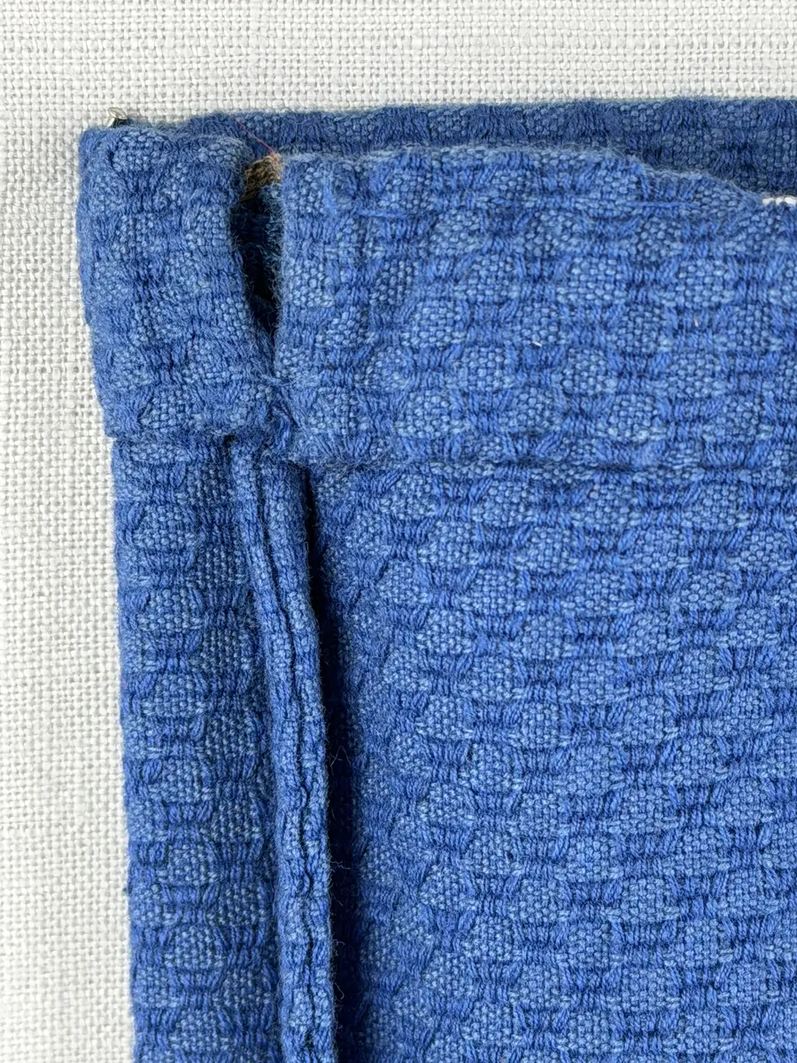 Tygpåse gjord av bomullsväv i sålldräll och broderi utfört med lingarn i korsstygn. Påsens öppning har en dragsko, 22mm bred dubbelvikt sydd med smygstygn, för förslutning med ett band. Påsen är hopsydd med vändsöm och raksöm.