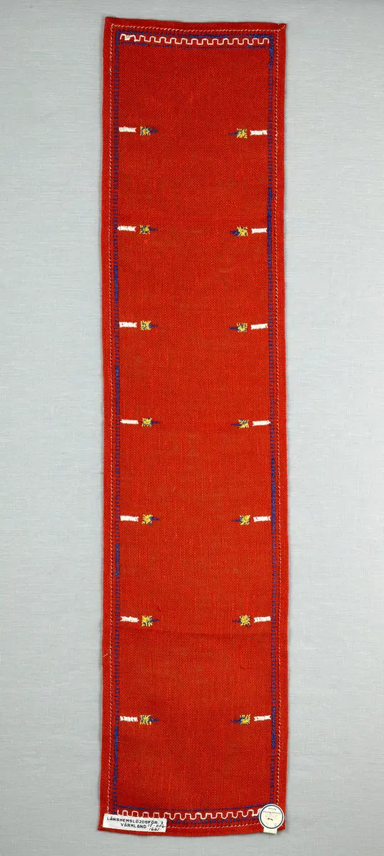 Jullöpare gjord av linneväv med 7tr/cm i tuskaft och broderi utfört med lingarn i stjälksöm, rutsöm, plattsöm samt korsstygn. 
Löparen är inramad med en korsstygns rad och kanterna har 9mm breda fållar runt om fastsydda med en halv hålsöm plus sneda hörn, vilka är sydda med kaststygn. 