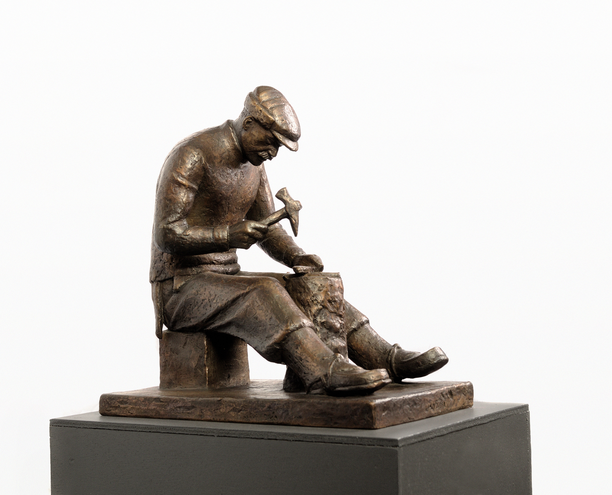 Mann med hamar/øks og brynestein, sitjande ved stabbe.