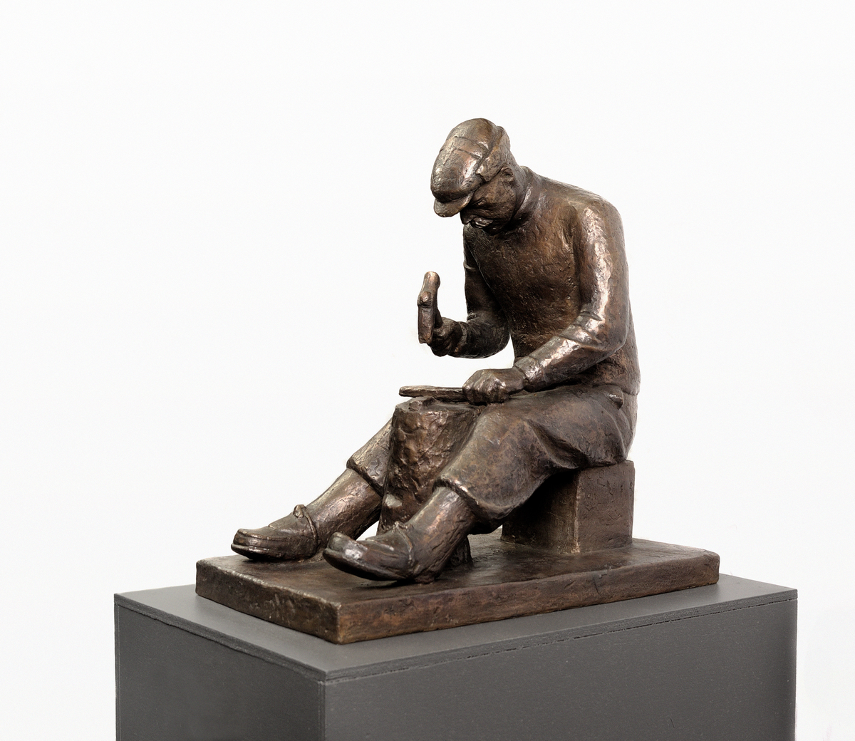 Mann med hamar/øks og brynestein, sitjande ved stabbe.