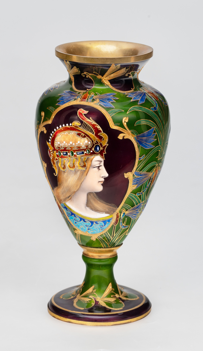 Vase i metall, dekorert med polykrom emalje og forgylt detaljering. Konisk korpus med kort hals og svakt utoverbrettet munningsrand. Vasen bæres av en kort stett med to vulster samt sirkulær hevet fotplate. Korpus er dekorert med et kvinnansikt, fremstilt i profil på burgundfarget bunn, iført kunstferdig hodepynt. Portrettet er omgitt av gullinnramming, samt organisk blomsterornamentikk på grønnfarget bunn.