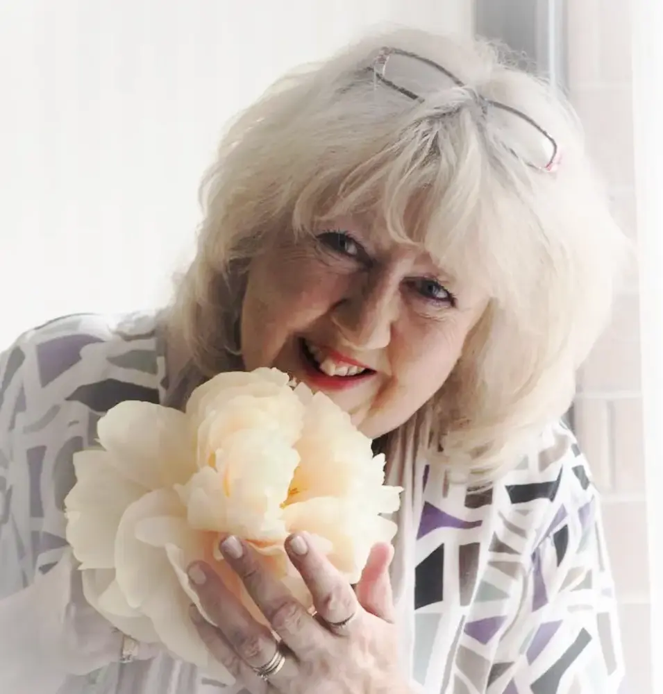 Kvinna med glasögon på huvudet håller en vit blomma framför ansiktet.