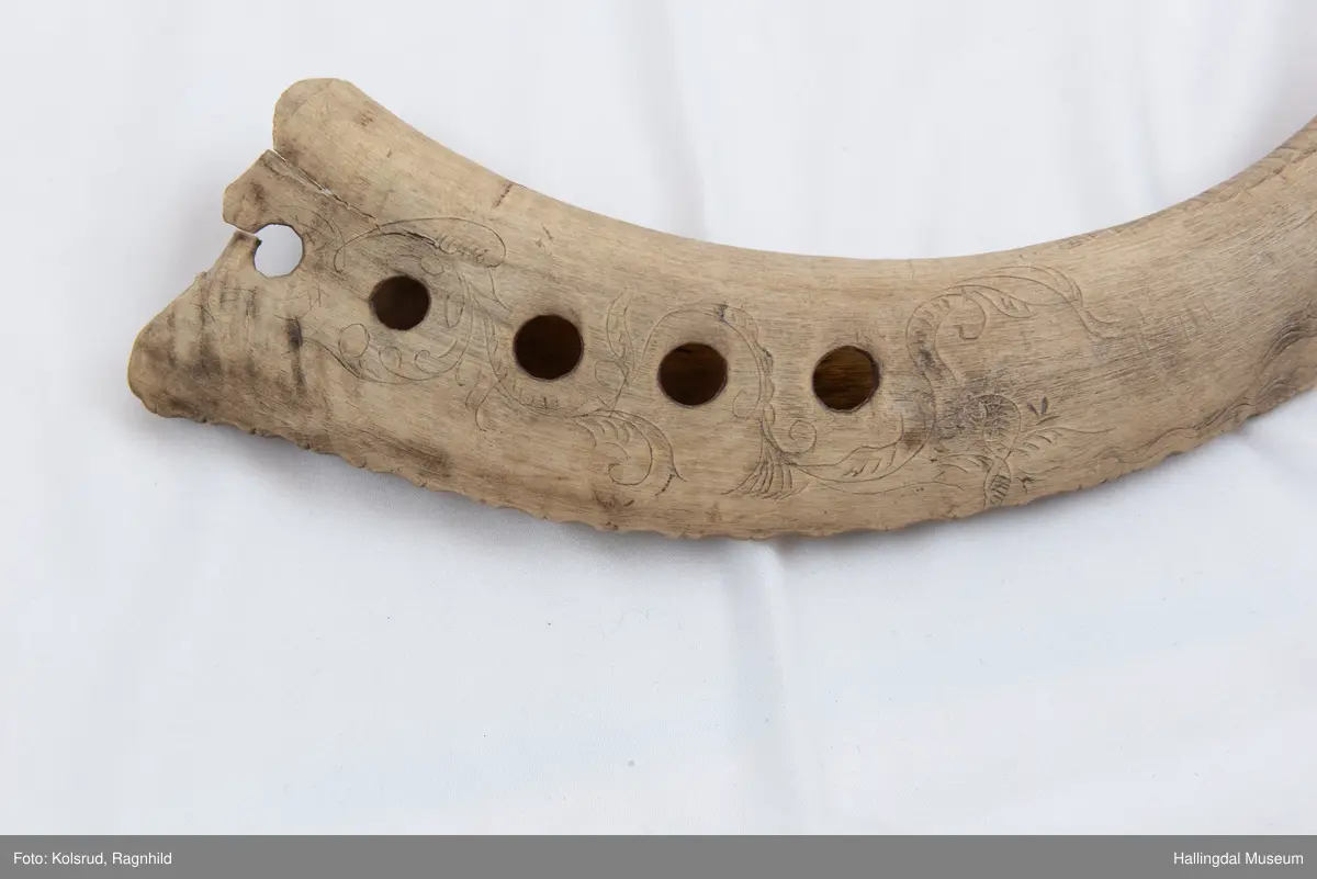 5 hol (bortimot sirkulære, ca. 1,1 cm i diameter) på eine sida og eitt mindre hol tvers gjennom hornet ytst i kanten lenger ut mot den smalaste enden. Rett avsaga i den smalaste enden, noko meir ujamn i andre enden. Bladornamentikk ripa inn med kniv. Bokstavane S T S er også ripa inn med kniv på kvar side. 