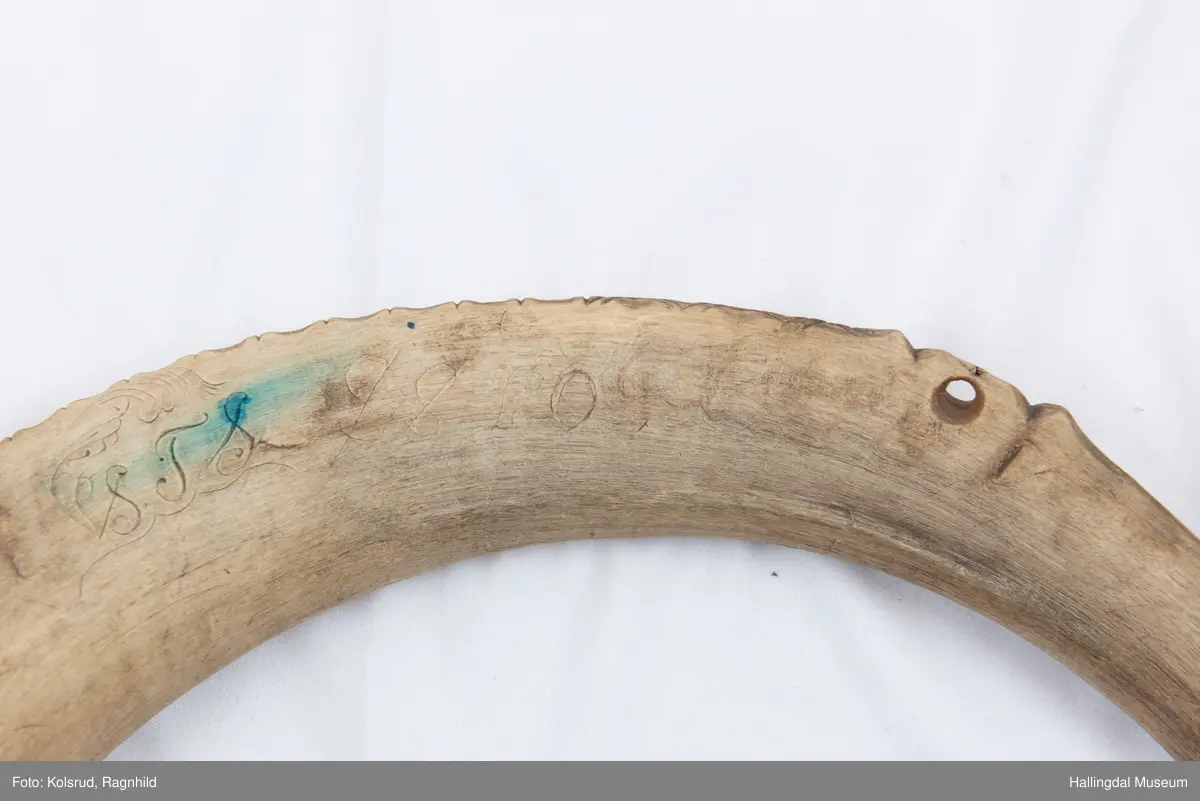 5 hol (bortimot sirkulære, ca. 1,1 cm i diameter) på eine sida og eitt mindre hol tvers gjennom hornet ytst i kanten lenger ut mot den smalaste enden. Rett avsaga i den smalaste enden, noko meir ujamn i andre enden. Bladornamentikk ripa inn med kniv. Bokstavane S T S er også ripa inn med kniv på kvar side. 