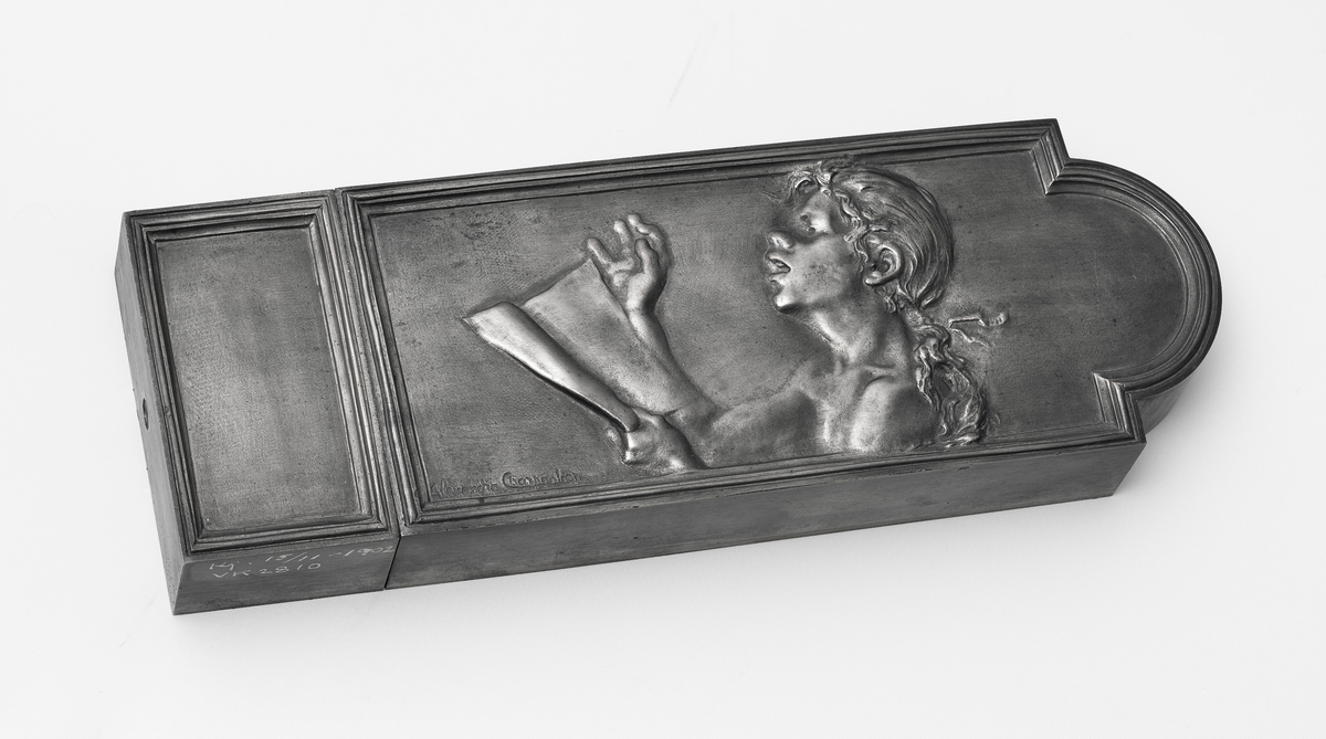 Rektangulært låsdeksel i støpt og fortinnet bronse. Horisontal grunnform bestående av låsekasse og sluttstykke. Forsiden viser en allegorisk fremstilling av en jente som synger, da som en personifisering av sangen.