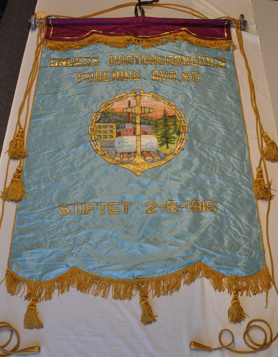 HM.030.1985-1: Tosidig fane i silketaft på råstang. Lys blå forside, mørk blå bakside. Fiolett kappe med blått, mønstret for. Gullfargede possementer, frynser i kappe og i fanedukens nederkant. Tre tunger i nederkant med dusker. FORSIDE: Sirkulært midtmotiv som viser fabrikkbygningen med tømmer og papirrull foran, omkranset av anker og kjetting. Tekst: ANKERS KARTONGARBEIDER / FORENING AVD. 85 / STIFTET 2 - 6 - 1918. BAKSIDE: Midtmotiv som viser et grantre med en oppadstigende sol bak. Foran står initialene NPF. Under ligger en hvit papirrull på en rød flate. Motiv omkranset av stilisert gullbård.Tekst: Medlemskap forplikter. 4 stk. bardunsnorer med dusk, 2 korte og 2 lange. 2 stk. styresnorer med dråpeformet håndtak.

HM.030.1985-2: Sidespyd, 2 stk., metall, formet som en skive med knott. Skrus på råstanga. D: 10 cm.

HM.0301985-3: Lærrem, for å feste fana til bærestang. Mørk brun. L: 98 cm, B: 1,5 cm.

HM.030.1985-4: Fanepose i lerret, gulhvit. 4 par bendelbånd i den åpne enden. . Skitten, flekkete. H: 249 cm, B: 135 cm.

HM.030.1985-5: Bærestang i 2 deler. Tre , metall. Påskrudd toppspyd i metall med initialene AKF i sjablongform. L: 143 cm (øvre del), 156 cm (nedre del).

HM.030.1985-6: Bardunsnor

HM.030.1985-7: Styresnor, 2 stk.